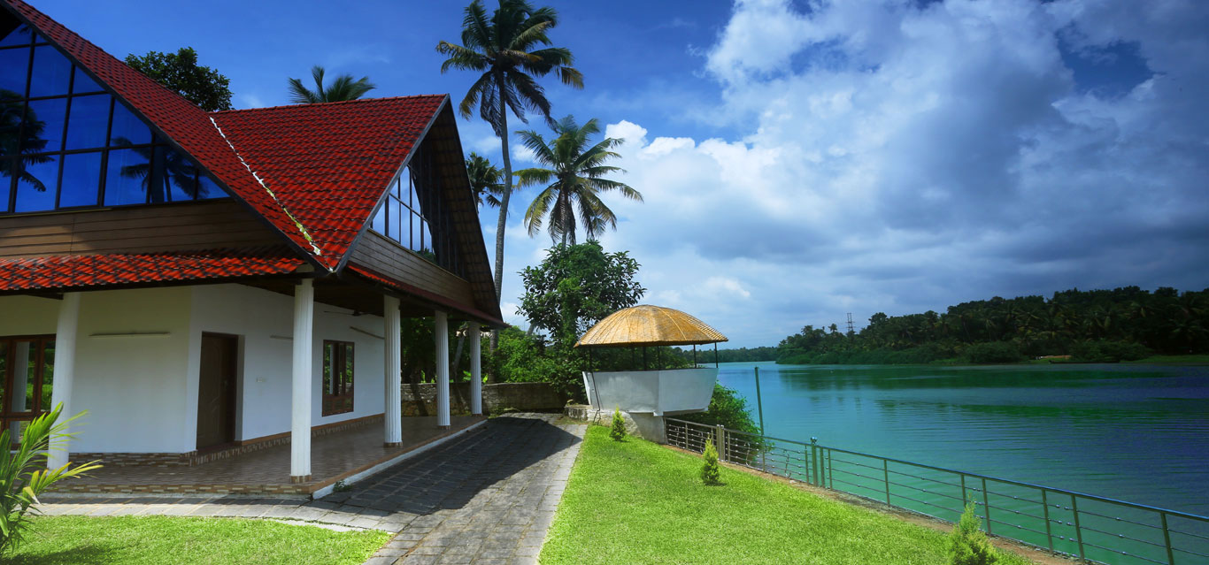 Red-roofed riverside cottage beside the Muvattupuzha River with coconut palms